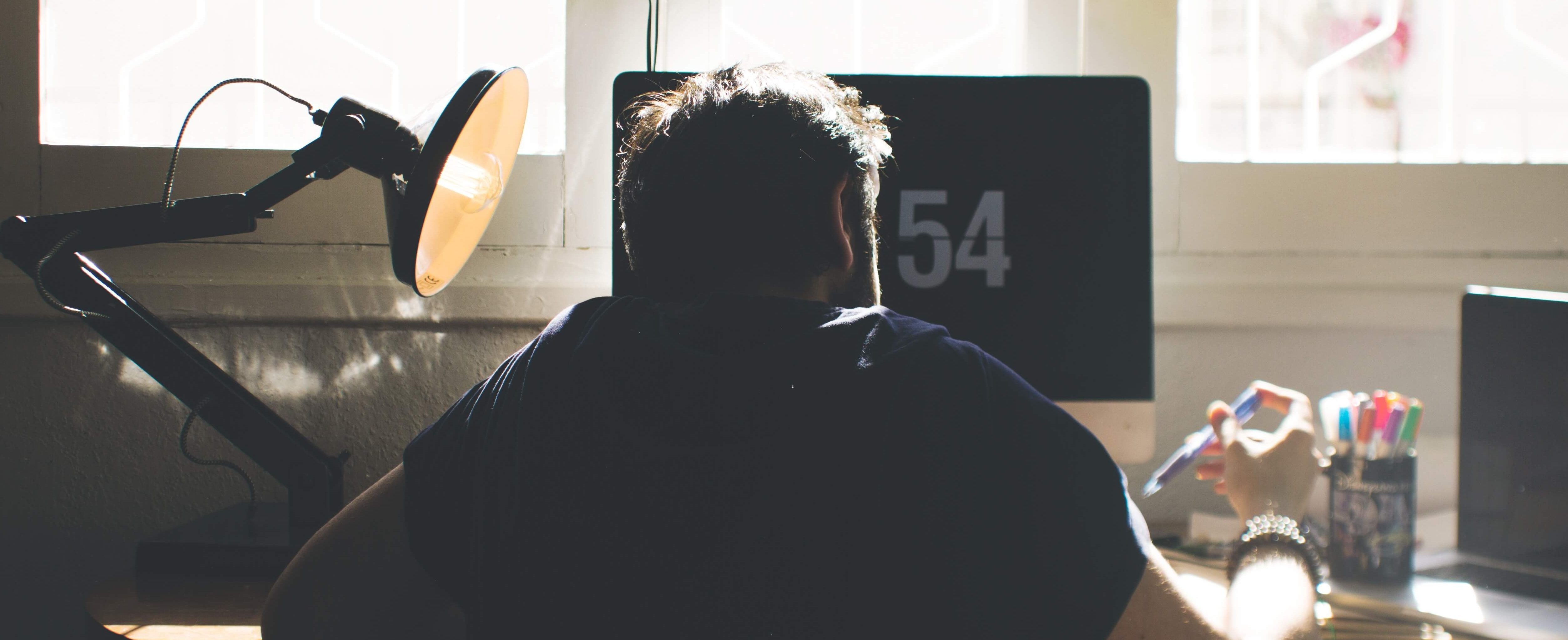 A back view of a man sitting at his full desk