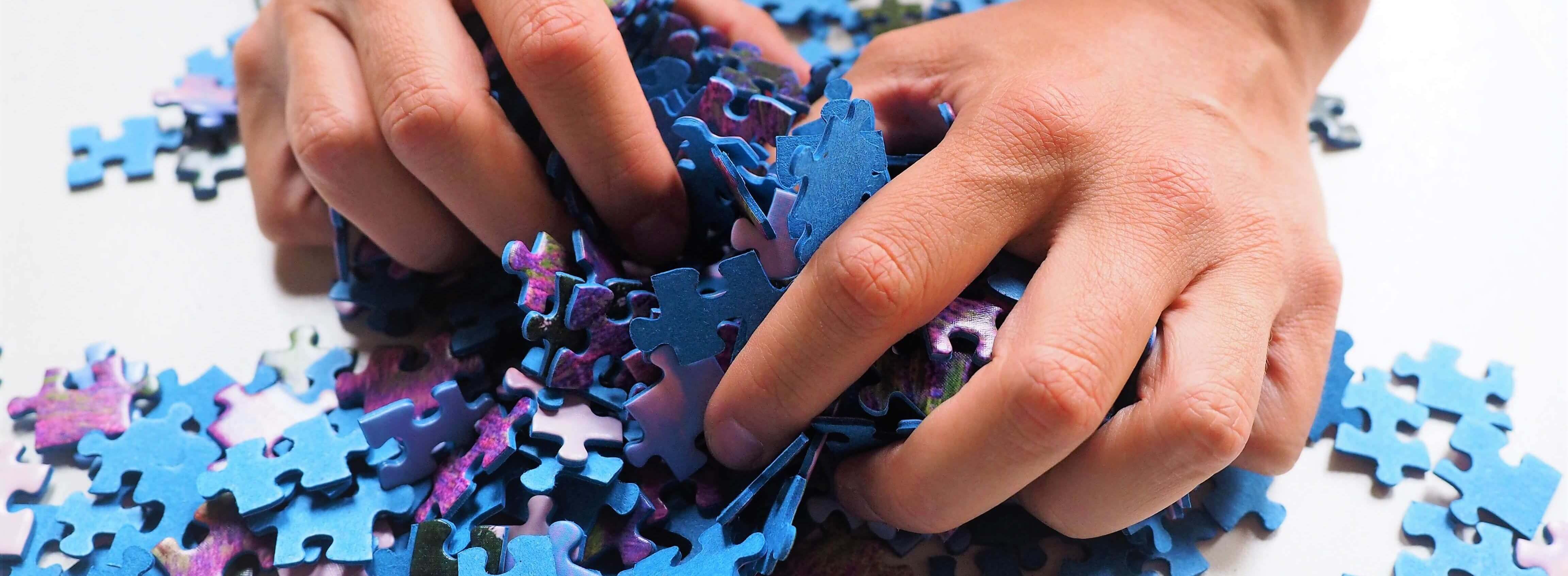 Hands grabbing and sorting through a mix of puzzle pieces