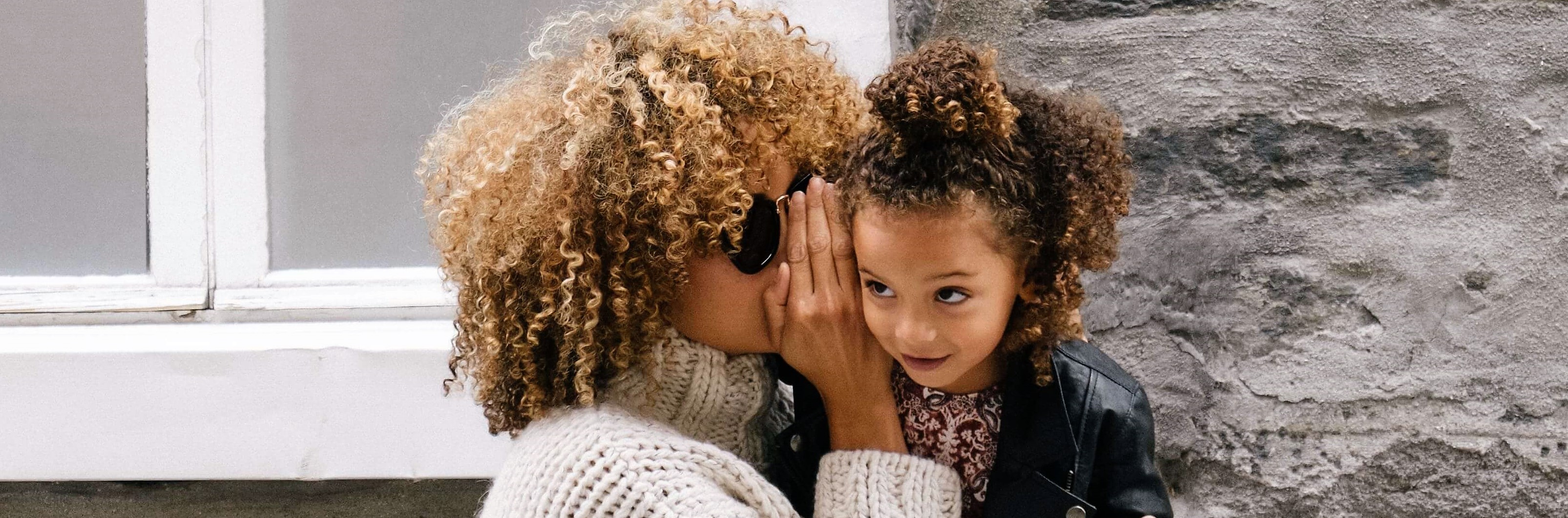 A woman whispering something into a curious girl's ear